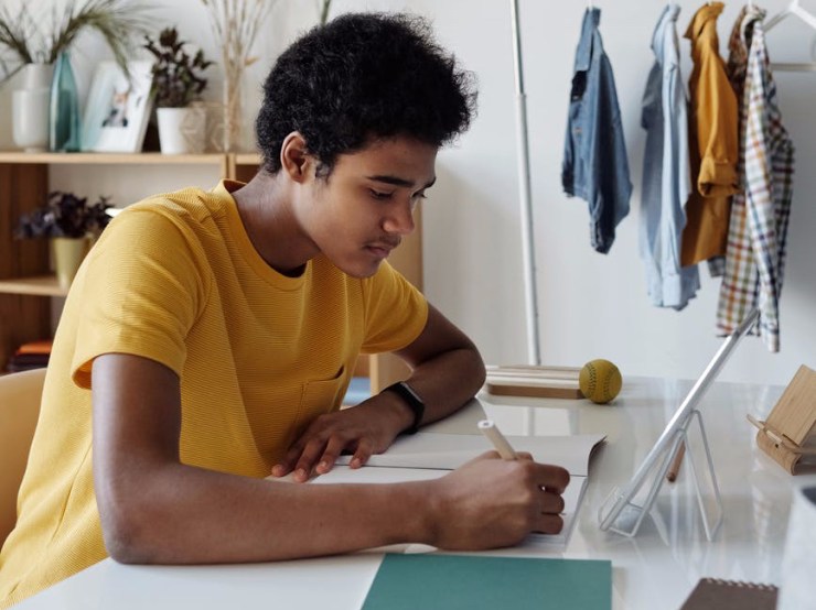 boy wearing yellow shirt while writing on white paper
