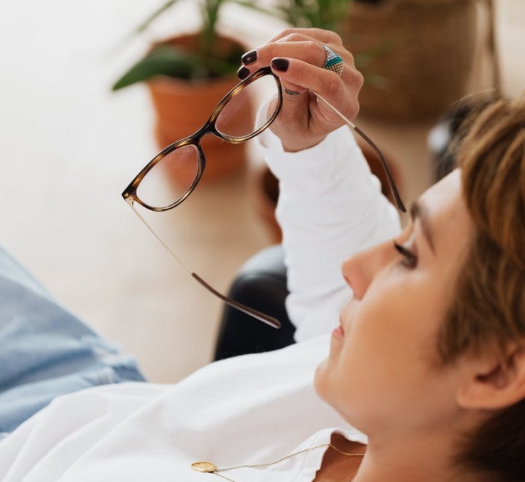 crop upset female sitting in armchair with eyeglasses in hand